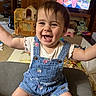 Violet is registered to the contest to win money with this photo: baby, casual_clothing, child, colorful, couch, cute, denim_overalls, furniture, happy, indoor, living_room, person, play_area, portrait, short_hair, sitting, smiling, television, toys, wooden_cabinet