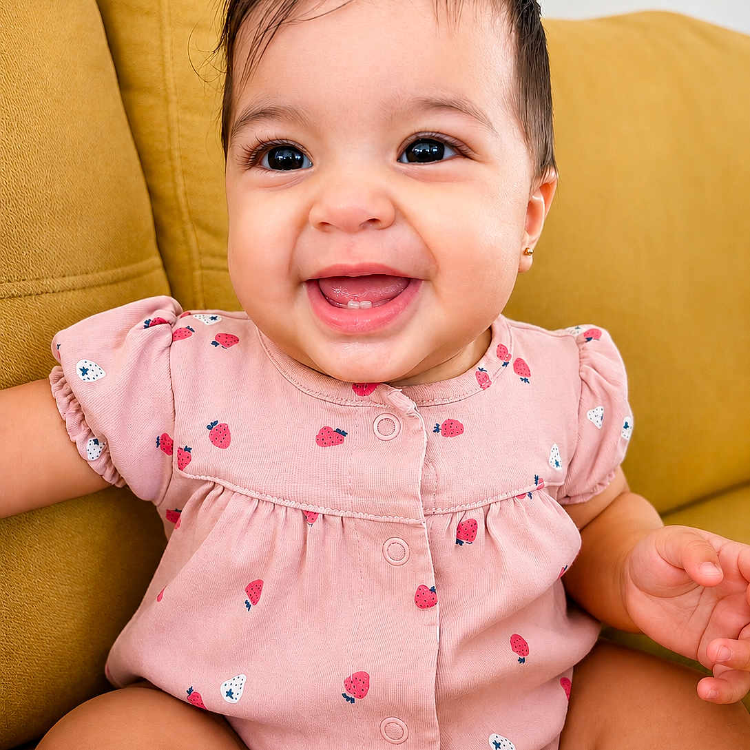 Renesmee joined the competition — help win amazing prizes! baby, child, smiling, pink_clothing, strawberry_pattern, couch, yellow_couch, happy, portrait, indoor, cute, infant, sitting, face, person, young_child, adorable, cheerful, skin, short_hair