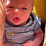 baby, infant, face, tongue_out, onesie, striped_clothing, tattoo, arm, hand, skin, sunlight, yellow_background, closeup, person, newborn, cute, expression, child, casual, indoor