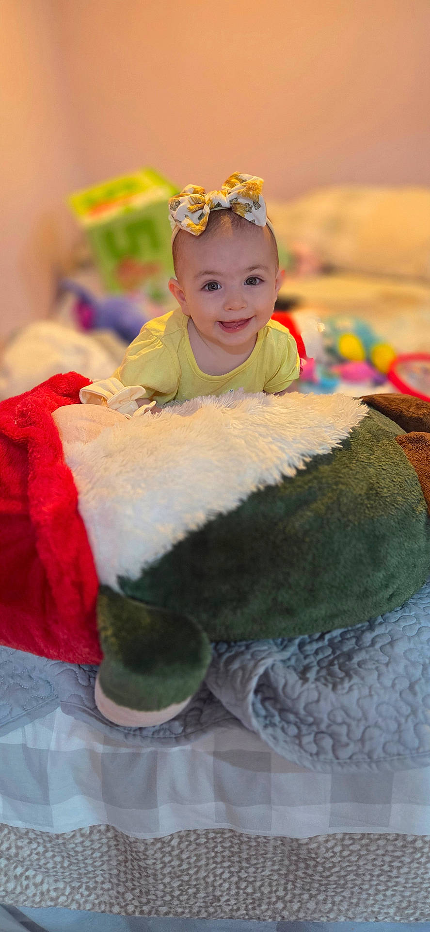 Tinatin is registered to the contest to win money with this photo: baby, bed, blanket, bow, child, cozy, cute, face, happy, headband, home, indoor, infant, person, plush_toy, portrait, smiling, soft_toy, yellow_clothing, young_child