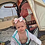 baby, child, pink_bow, headband, beach, tent, towel, stroller, sand, outdoor, curious, expression, clothing, blanket, sunshade, infant, person, portrait, casual, relaxed