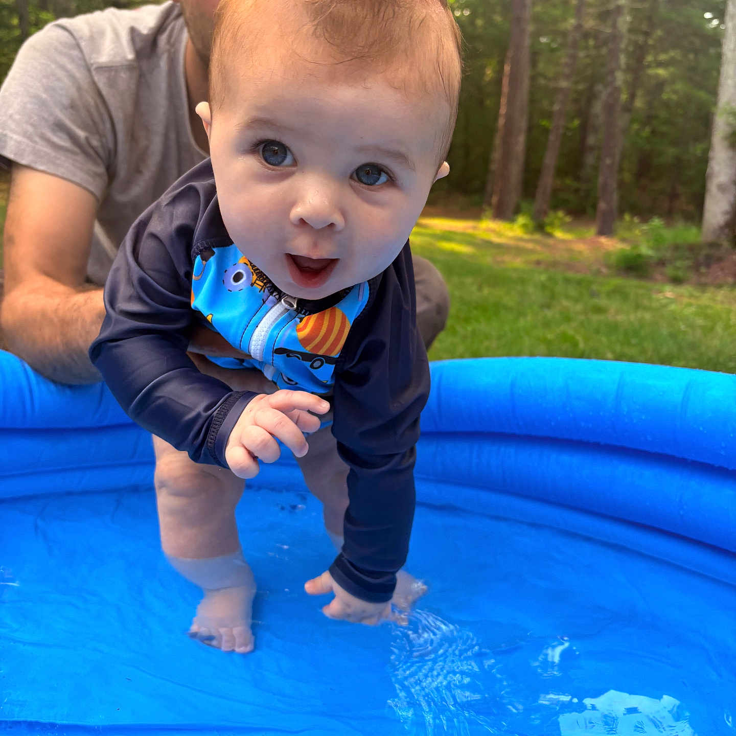 Noah is registered to the contest to win money with this photo: adult, baby, blue, child, expression, fun, grass, happy, nature, outdoor, person, play, pool, splash, summer, sunlight, support, swimwear, trees, water