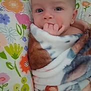 Athena is registered to the contest to win money with this photo: baby, blanket, pillow, flower_pattern, infant, hand, face, wrapped, cozy, cute, child, skin, expression, indoors, portrait, young, sucking_fingers, colorful, soft, comfort