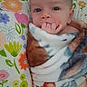 baby, blanket, pillow, flower_pattern, infant, hand, face, wrapped, cozy, cute, child, skin, expression, indoors, portrait, young, sucking_fingers, colorful, soft, comfort