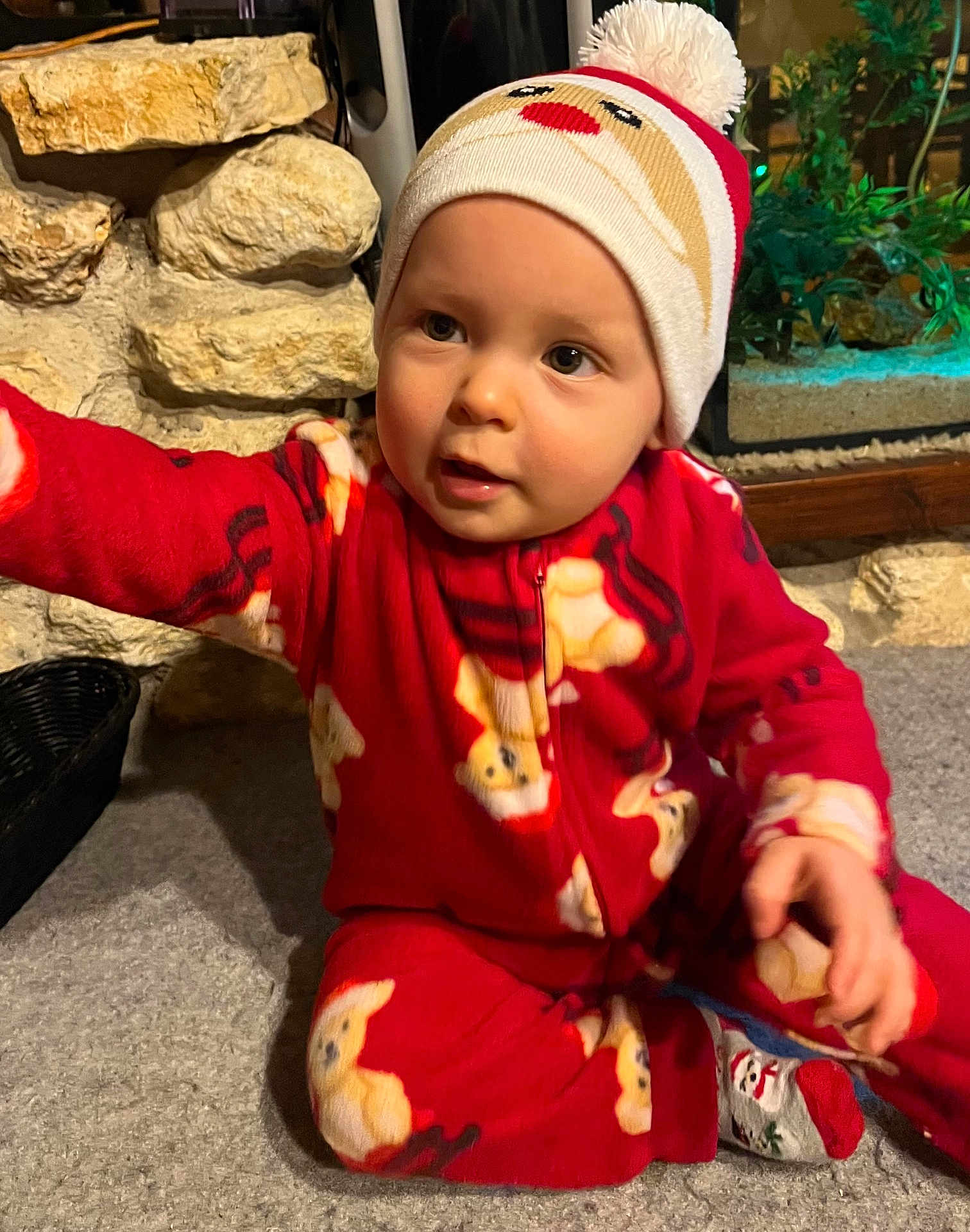Lino participe au concours pour gagner de l'argent avec cette photo : baby, child, pajamas, red_clothing, hat, santa_hat, teddy_bear_pattern, carpet, stone_wall, aquarium, indoor, cute, smiling, person, holiday, festive, winter_clothing, sitting, reaching, cozy