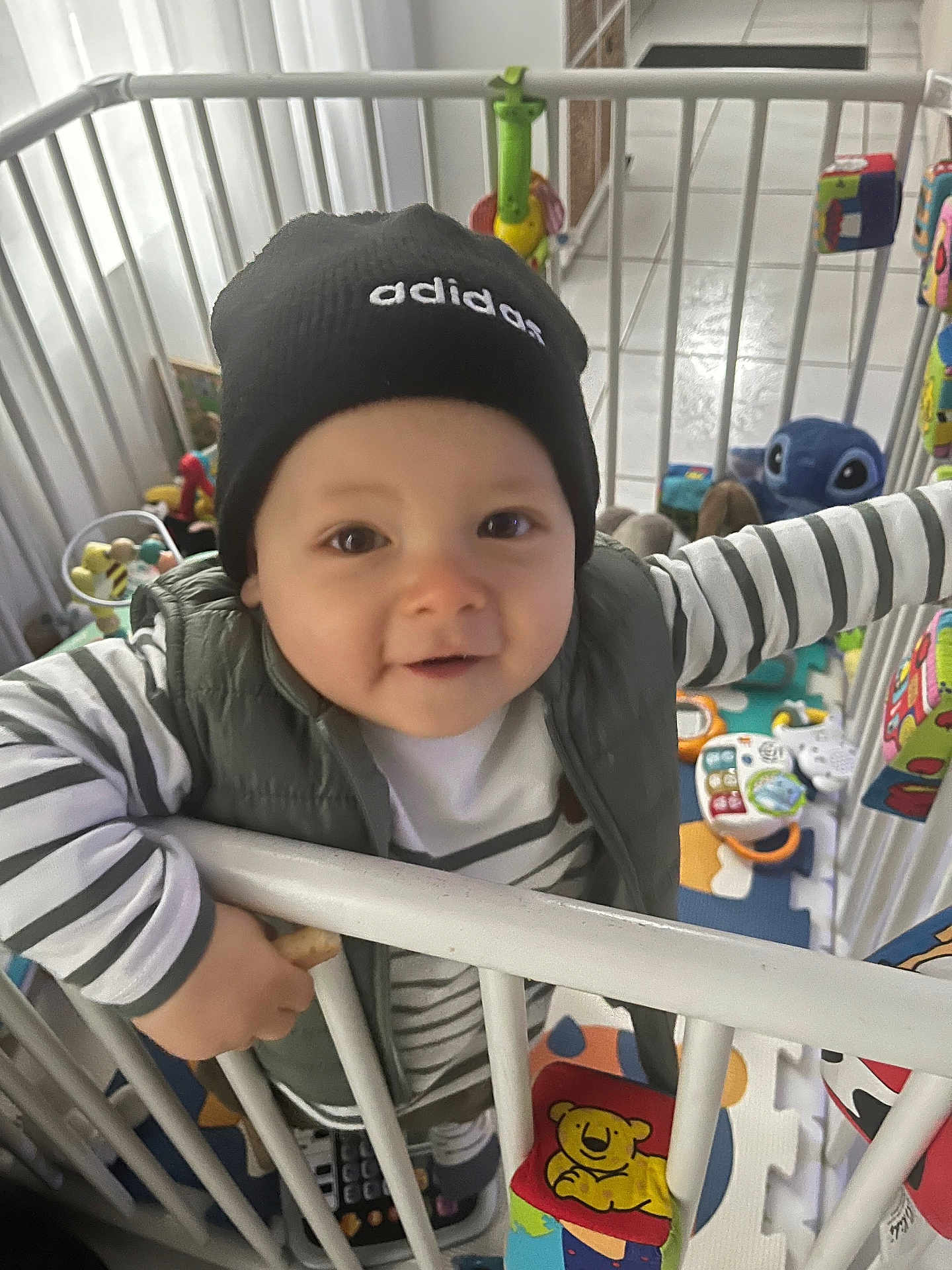 Lino participe au concours pour gagner de l'argent avec cette photo : toddler, child, beanie, adidas, striped_shirt, playpen, toys, smiling, indoor, colorful, baby, clothing, hand, face, person, play_area, plastic, floor_mat, cute, happy