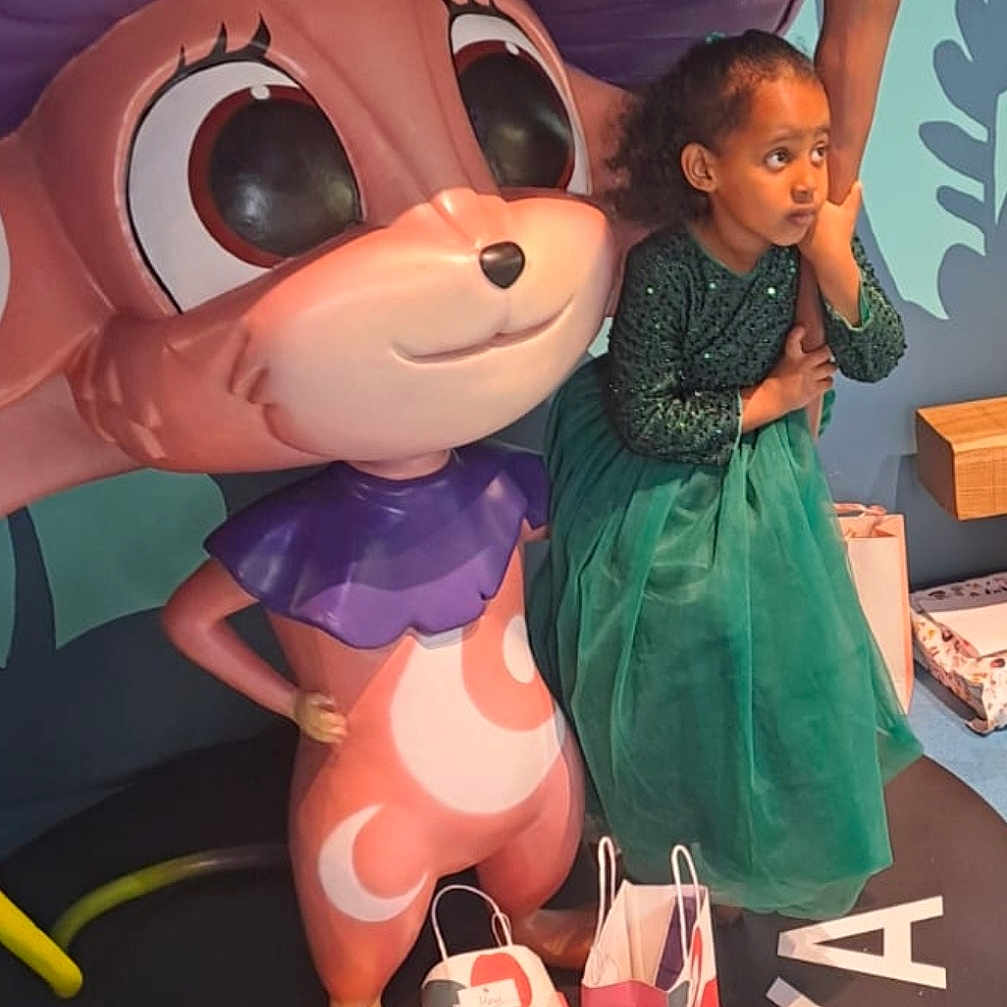 Hayat a rejoint le concours — aidez-le/la à gagner de superbes lots ! accessories, baby, bag, child, clothing, dress, face, female, footwear, girl, handbag, head, hugging, indoors, person, photography, portrait, shoe, text, toy