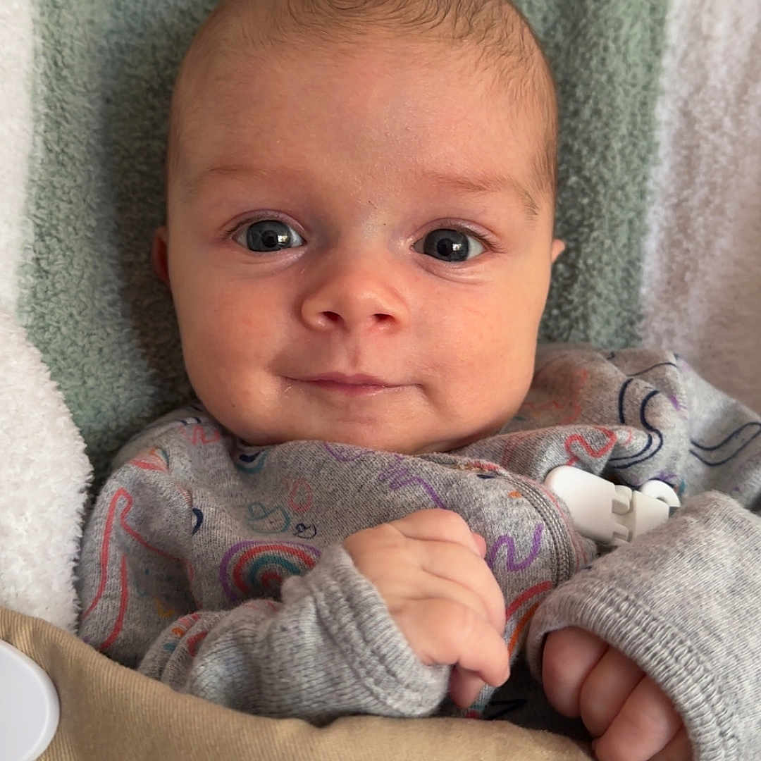 Liam is registered to the contest to win money with this photo: baby, bib, blanket, closeup, clothing, cozy, cute, expression, eyes, face, hands, head, infant, newborn, portrait, skin, sleeves, smile, soft, striped_blanket