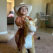 Alfredo joined the competition — help win amazing prizes! toddler, child, cowboy_hat, rocking_horse, plush_toy, indoor, carpet, smiling, happy, toy, furniture, living_room, childhood, play, cute, person, floor, home, casual_clothing, fun