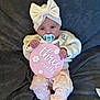 baby, infant, pacifier, headband, bow, pink, sign, three_months, blanket, sweater, pants, floral_pattern, cute, lying_down, child, adorable, soft_texture, clothing, indoor, portrait