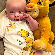 Noah is registered to the contest to win money with this photo: baby, infant, plush_toy, simba, lion_king, onesie, clothing, couch, soft_toy, cute, child, person, smiling, face, indoor, comfort, furniture, sitting, closeup, happy