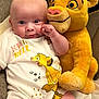 baby, infant, plush_toy, simba, lion_king, onesie, clothing, couch, soft_toy, cute, child, person, smiling, face, indoor, comfort, furniture, sitting, closeup, happy