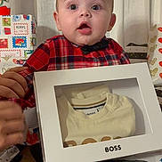 Isaac a rejoint le concours — aidez-le/la à gagner de superbes lots ! baby, celebration, child, clothing, curtain, expression, floor, gift_box, hands, holiday, home, indoor, packaging, person, plaid_shirt, portrait, present, socks, surprised, young_child