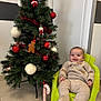 baby, child, smiling, christmas_tree, ornaments, gingerbread_man, candy_cane, green_chair, knit_outfit, indoor, holiday, festive, decorations, floor_tiles, wall, cozy_clothing, happy, person, seat, holiday_season