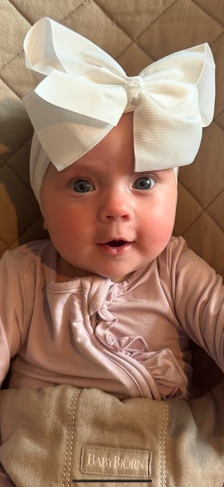 Collins joined the competition — help win amazing prizes! baby, child, headband, bow, pink_clothing, face, eyes, mouth, skin, soft_texture, quilted_surface, babybjorn, close_up, infant, cute, portrait, indoors, resting, headwear, apparel