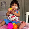 Anna Chin is registered to the contest to win money with this photo: toddler, child, indoor, toy, ball, bed, medical_patch, clothing, foot, person, furniture, door, curtains, shirt, shorts, cute, playing, sitting, colorful, young