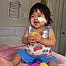 bed, child, clothing, colorful_balls, cute, door, face, furniture, happy, indoor, patch, person, plastic_ball, playful, room, sitting, smiling, toddler, towel, toy