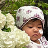 Anna is registered to the contest to win money with this photo: baby, child, flower, hydrangea, greenery, leaf, nature, outdoor, face, headwear, floral_pattern, plant, cute, garden, portrait, infant, skin, expression, soft_light, closeup