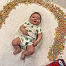 baby, infant, onesie, shamrock, cereal, lucky_charms, cereal_box, blanket, smiling, lying_down, colorful, food, breakfast, happy, child, indoors, toy, cute, playful, st_patricks_day