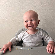 Wes is registered to the contest to win money with this photo: baby, child, high_chair, food, messy, smiling, face, hands, infant, feeding, indoor, clothing, long_sleeve, table, expression, cute, portrait, skin, person, happy