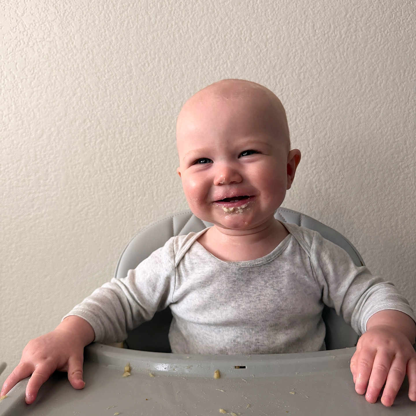 Wes is registered to the contest to win money with this photo: baby, child, high_chair, food, messy, smiling, face, hands, infant, feeding, indoor, clothing, long_sleeve, table, expression, cute, portrait, skin, person, happy