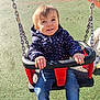 child, toddler, swing, playground, metal_chain, jacket, puffer_jacket, jeans, smile, happy, seat, park, outdoor, sunlight, rubber_surface, play_equipment, hands, portrait, young_child, weekend_fun
