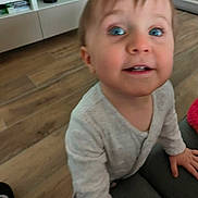 Candice participe au concours pour gagner de l'argent avec cette photo : child, toddler, baby, blue_eyes, face, smile, indoor, wooden_floor, sofa, furniture, onesie, hand, portrait, close_up, blurry, living_room, television, curious, hair, skin