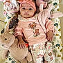 baby, child, infant, plush_toy, headband, pink_clothing, deer_print, patterned_cushion, stuffed_animal, rabbit_toy, toddler, cute, soft_toy, lying_down, indoors, portrait, smiling, hand, face, young_child
