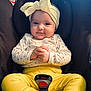 baby, child, car_seat, yellow_pants, headband, smiling, hands_clasped, cute, infant, clothing, socks, seatbelt, indoors, portrait, happy, small_child, cute_expression, baby_fashion, close_up, adorable
