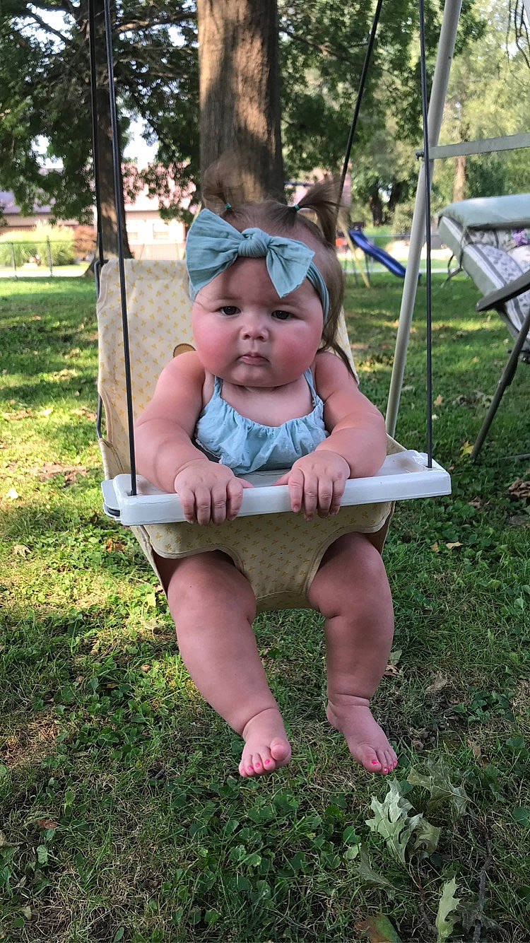 Vivienne is registered to the contest to win money with this photo: baby, baby_toddler_clothing, chair, eye, face, grass, hairstyle, hand, happy, head, headwear, human_body, lap, leisure, outdoor_furniture, person, pink, plant, recreation, swing