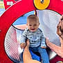 baby, child, playground, slide, red, blue, striped_clothing, smiling, happy, person, adult_hand, outdoor, metal, play_equipment, park, fun, circular_tunnel, cute, holding, sitting