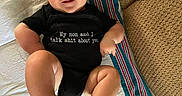 Ryker joined the competition — help win amazing prizes! baby, infant, onesie, text_on_clothing, striped_blanket, couch, cushion, barefoot, skin, smiling, face, head, blue_eyes, lying_down, indoor, person, child, cute, expression, furniture
