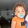 Kimoni joined the competition — help win amazing prizes! toddler, child, pacifier, orange_shirt, curly_hair, indoor, person, face, expression, baby, young_child, cute, portrait, casual_clothing, holding, blurred_background, eyes, skin, head, short_sleeve