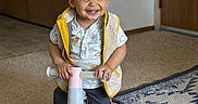 Kimoni is registered to the contest to win money with this photo: toddler, child, smiling, tricycle, indoor, carpet, vest, curly_hair, happy, toy, floor, rug, shirt, person, home, play, baby, cute, young_child, furniture