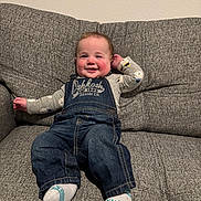 Roman joined the competition — help win amazing prizes! baby, child, smiling, denim_overalls, socks, couch, indoor, happy, cute, person, seated, clothing, face, head, young_child, long_sleeve_shirt, home, infant, casual, portrait