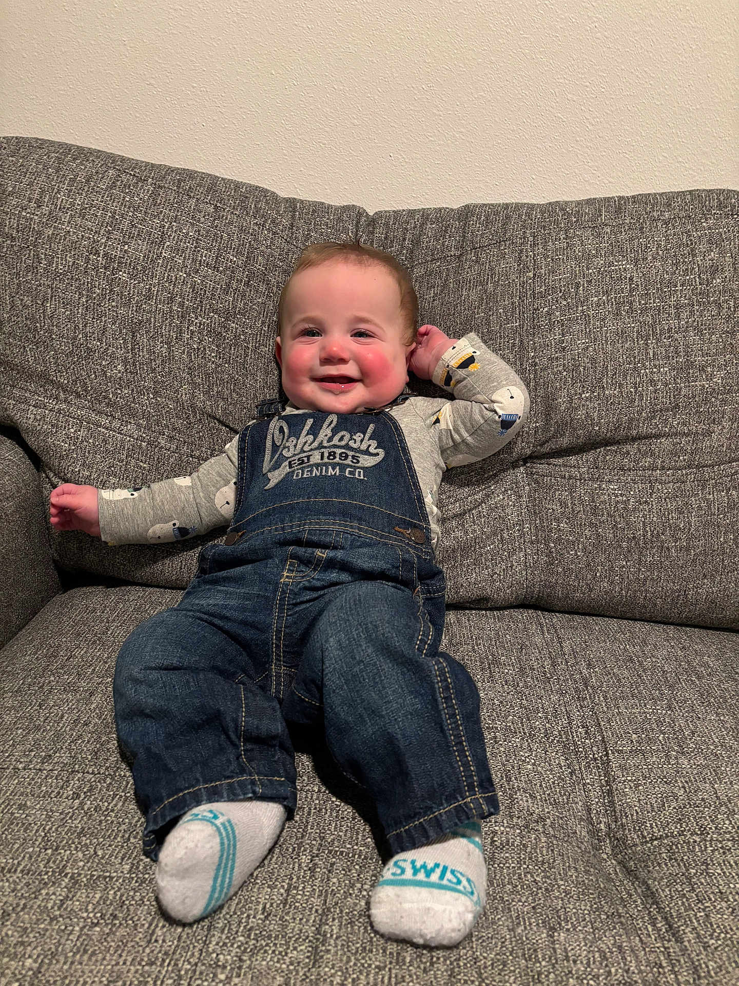 Roman joined the competition — help win amazing prizes! baby, child, smiling, denim_overalls, socks, couch, indoor, happy, cute, person, seated, clothing, face, head, young_child, long_sleeve_shirt, home, infant, casual, portrait