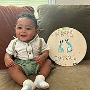 Josiah is registered to the contest to win money with this photo: baby, celebration, child, couch, cute, decor, easter_sign, footprints, green_shorts, happy, home, indoor, infant, portrait, seated, shirt, smiling, socks, suspenders, window_blinds