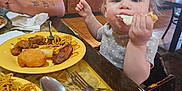 Selene is registered to the contest to win money with this photo: baby_food, casual_clothing, child, cute, dining, eating, food, fork, furniture, high_chair, interior, noodles, person, plate, reflection, restaurant, spoon, table, tattoo, toddler