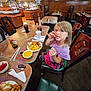 casual, chair, child, cutlery, dining, drink, food, fried_food, girl, indoor, meal, napkin, noodles, purple_shirt, restaurant, skirt, soup, table, television, wooden_chair