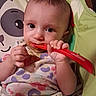 baby, child, spoon, high_chair, messy, cute, eating, infant, face, hand, clothing, pattern, colorful, indoor, seat, food, feeding, person, expression, mealtime