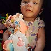 Aurora is registered to the contest to win money with this photo: baby, child, clothing, colorful, comfort, cozy, cute, hand, indoor, infant, patterned, person, plush, portrait, sitting, soft_toy, stuffed_toy, toy, unicorn, young_child