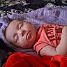 baby, sleeping, towel, blanket, bed, coral_shirt, face, infant, child, resting, indoors, patterned_bedspread, peaceful, soft_texture, cozy, pink, red, purple, person, young_child