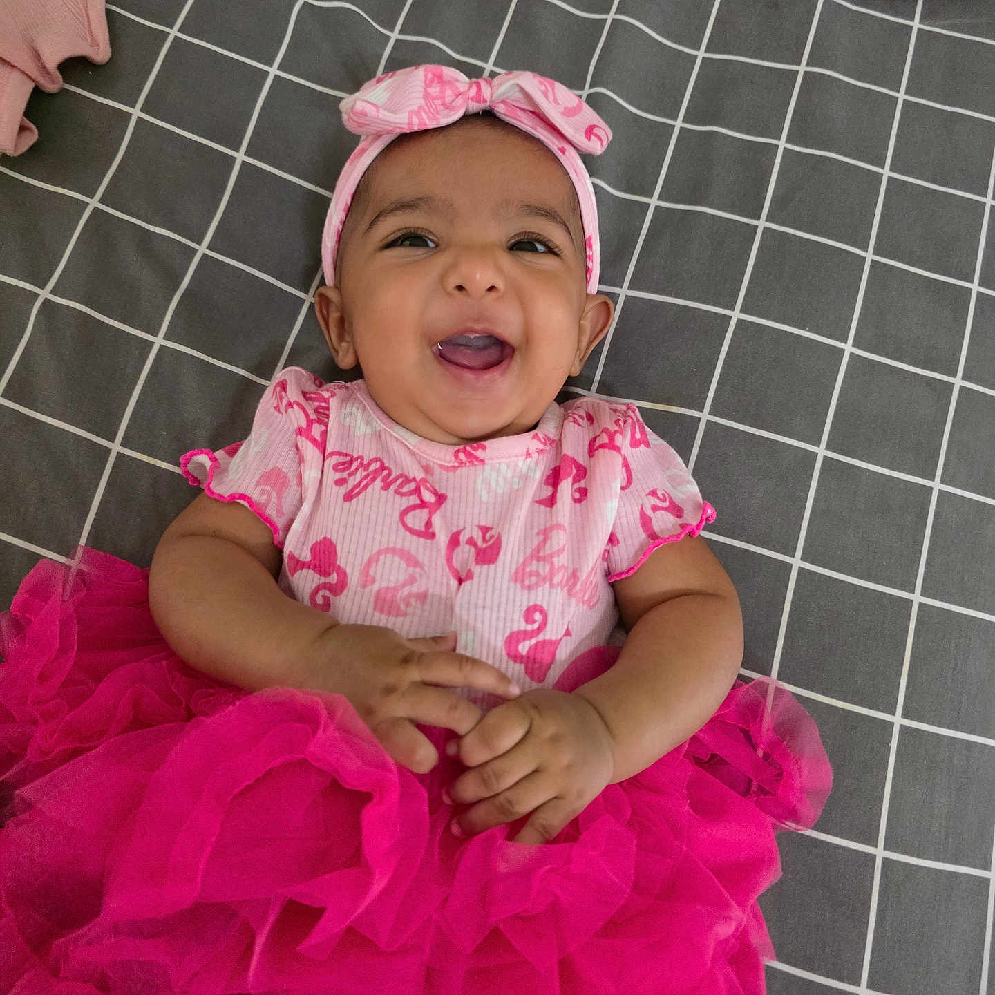 Nisa is registered to the contest to win money with this photo: baby, bedspread, checkered, cheerful, child, clothing, cute, fashion, hands, happy, headband, indoors, infant, lying_down, person, pink, portrait, smiling, tutu, young_child