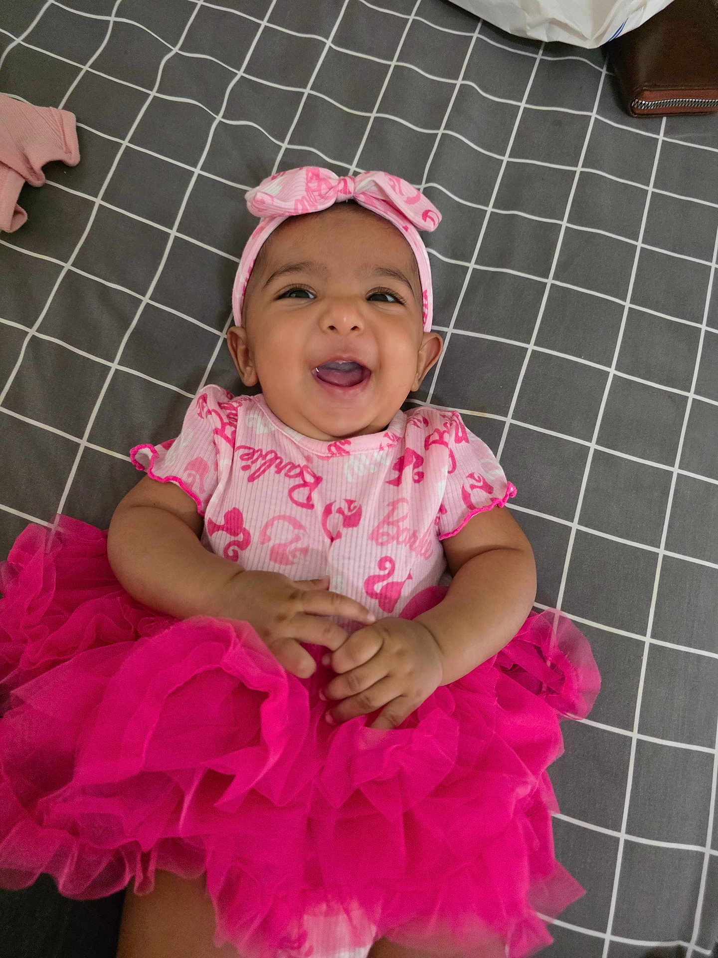 Nisa is registered to the contest to win money with this photo: baby, bedspread, checkered, cheerful, child, clothing, cute, fashion, hands, happy, headband, indoors, infant, lying_down, person, pink, portrait, smiling, tutu, young_child