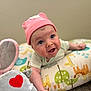 baby, infant, pink_hat, plush_toy, elephant_toy, heart_patch, colorful_pillow, animal_print, giraffe, lion, green_leaves, blue_bird, striped_clothing, cute, expression, indoors, soft_toys, child, face, curious