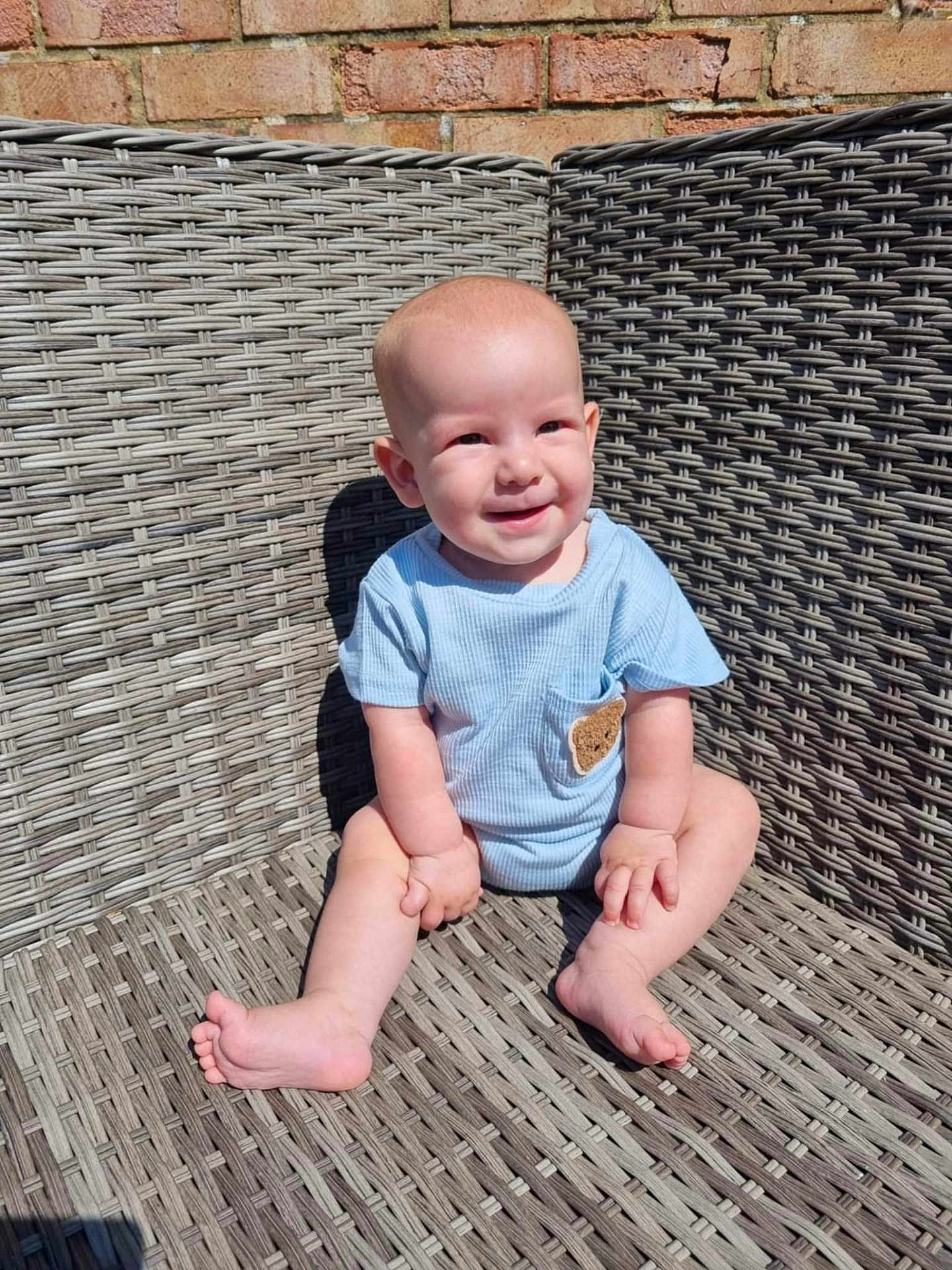 Sonny joined the competition — help win amazing prizes! baby, smiling, blue_clothing, outdoor, wicker_chair, brick_wall, sunlight, happy, sitting, infant, cute, child, portrait, skin, barefoot, small_hands, small_feet, texture, seat, shadow