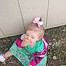 Astella is registered to the contest to win money with this photo: building_wall, casual_clothing, child, colorful_jacket, eating, grass, green_dress, ground, hand, happy, nature, outdoor, person, pink_bow, playful, rocks, summer, toddler, white_shoes, yellow_fruit