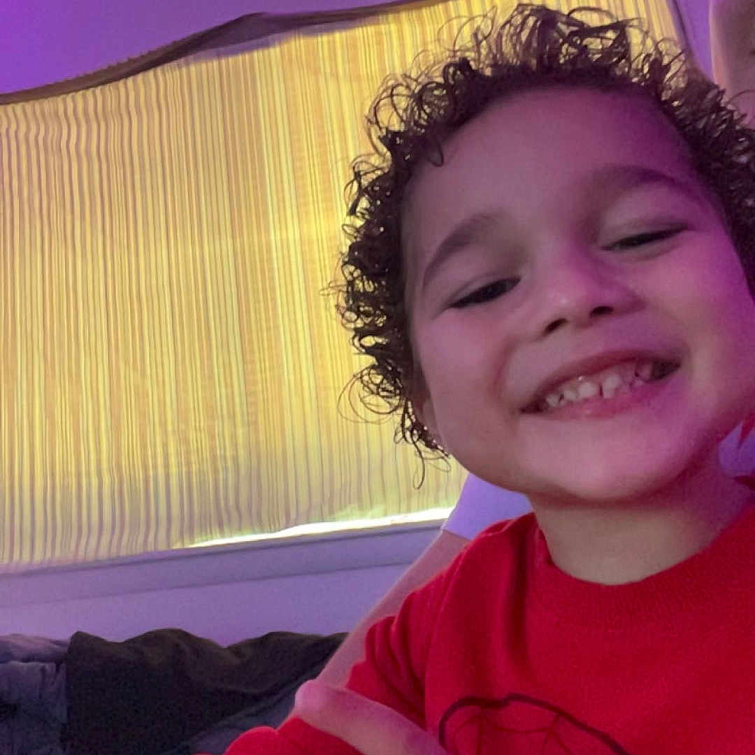 Jordan joined the competition — help win amazing prizes! candid, casual_clothing, cheerful, child, cozy, curly_hair, curtain, face, happy, human, indoor, led_lights, person, pointing, portrait, purple_light, red_sweater, smile, window, young_child