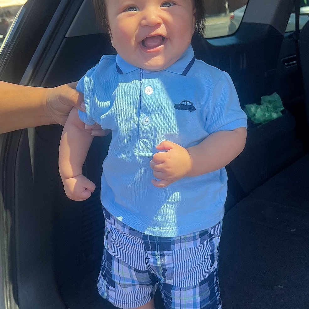 Uvaldo Jr joined the competition — help win amazing prizes! baby, blue_shirt, car, car_trunk, child, clothing, cute, daylight, hand, happy, human, outdoor, person, plaid_shorts, portrait, smiling, socks, standing, sunlight, toddler