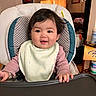 Moana is registered to the contest to win money with this photo: baby, bib, child, clothing, curtains, face, furniture, hair, happy, high_chair, home, indoor, infant, person, portrait, room, seat, smile, table, window